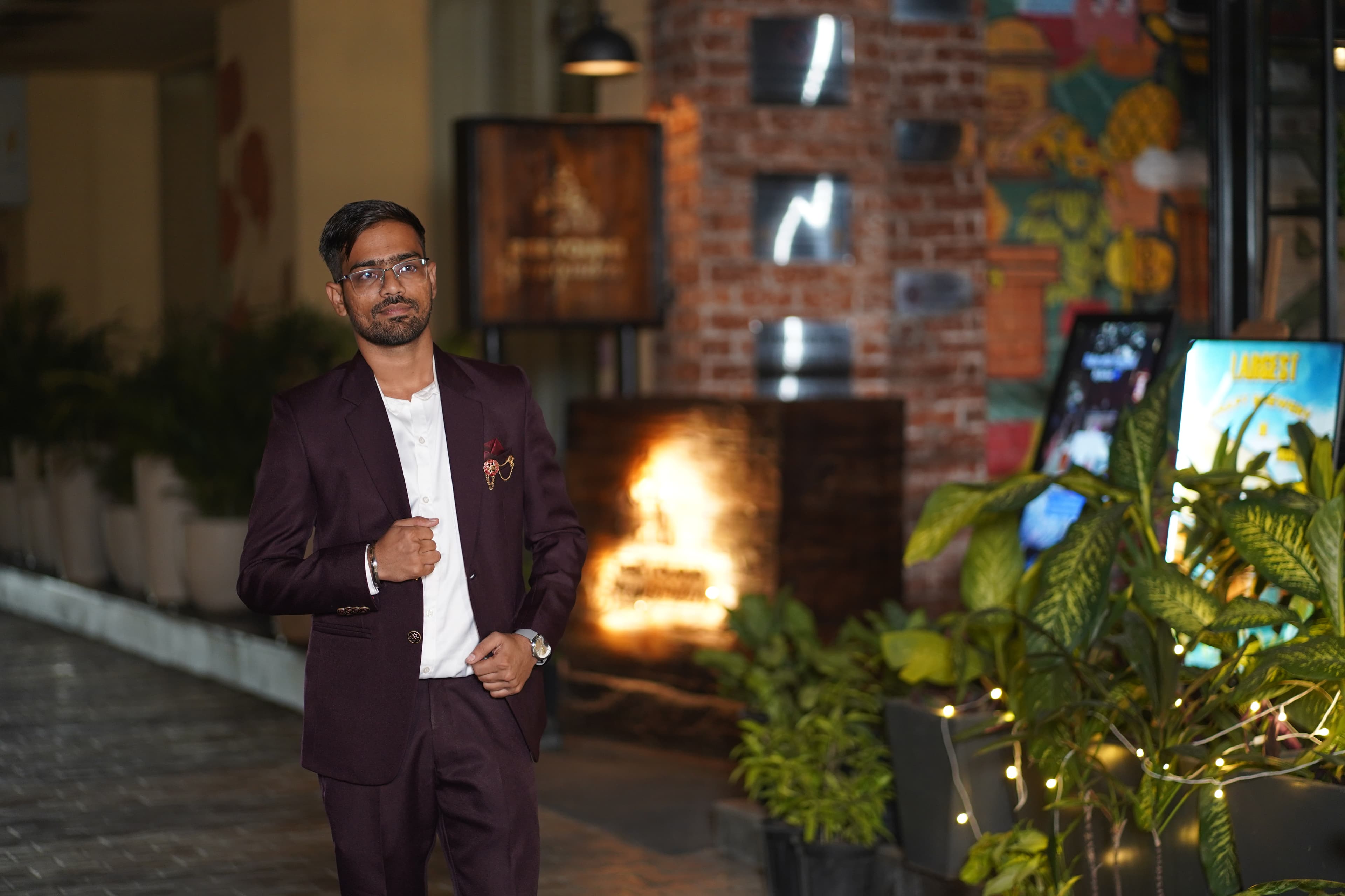 Groom portrait in burgundy suit with warm fairy-light backdrop